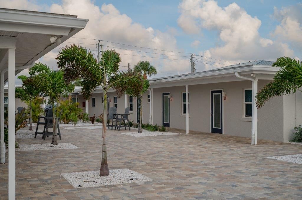 Modern courtyard with young trees, white buildings, and a paved patio under cloudy skies