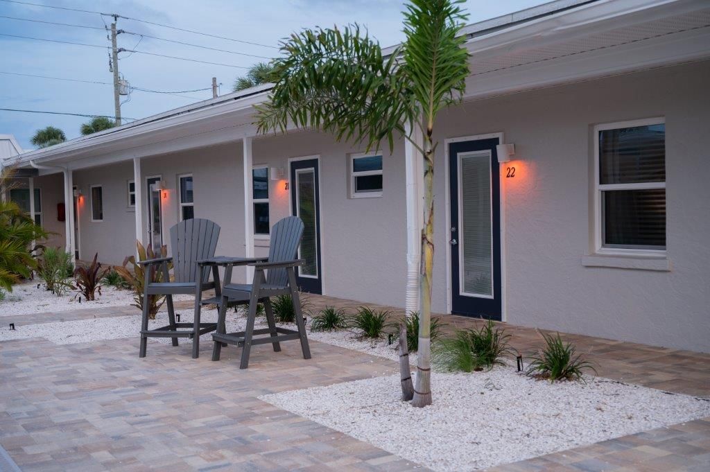 Modern motel-style building with patio seating, lit doorways, and a small palm tree in front