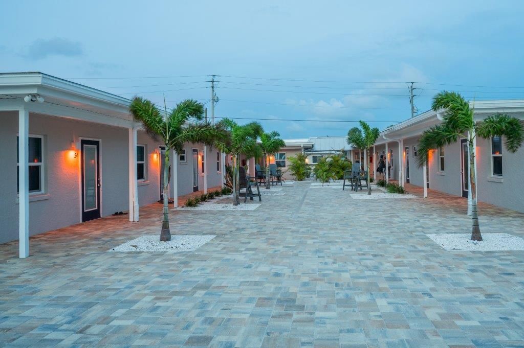 Palm-lined stone walkway between low white buildings at dusk under a blue sky