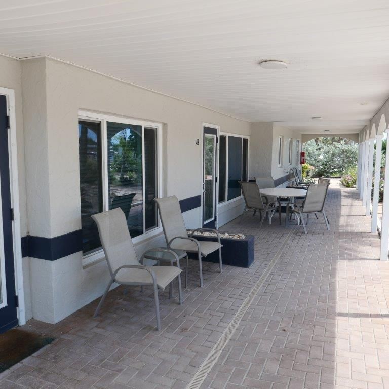 Covered outdoor walkway with chairs, tables, and windows along a beige building