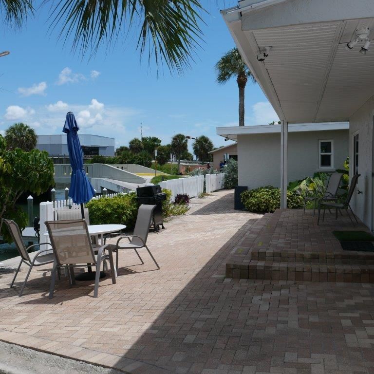Patio with table, chairs, blue umbrella, potted plants, and white house exterior on a sunny day