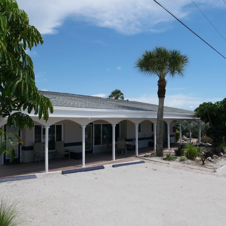 Single-story white house with arched porch, palm tree, and clear blue sky