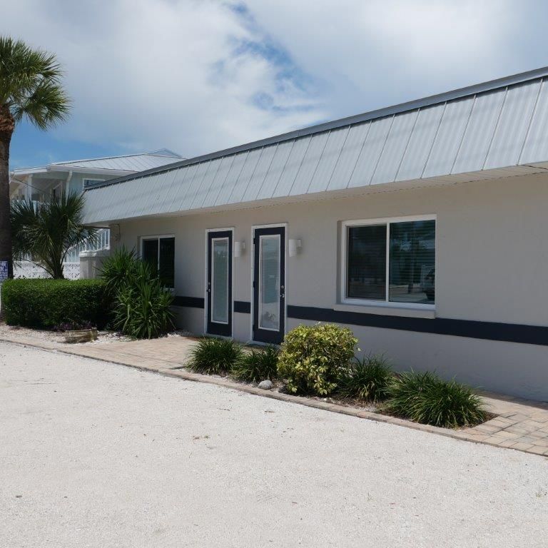 Low white building with two doors, windows, and landscaping under a bright sky