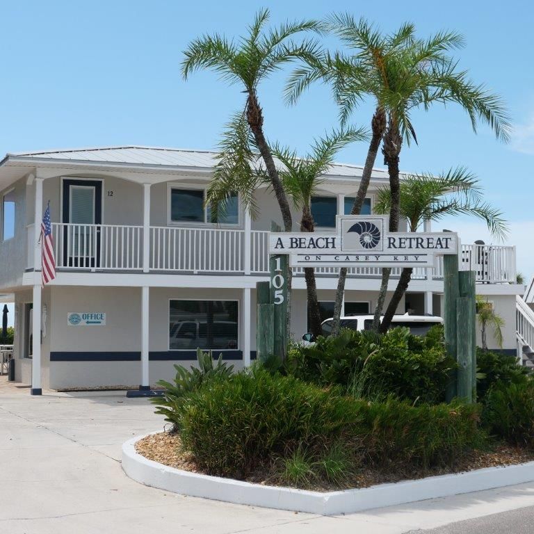 Beach retreat building with palm trees, white balcony, and sign reading “A Beach Retreat”