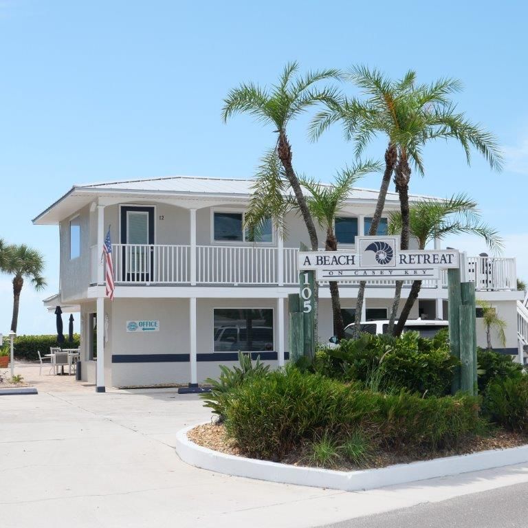 Beach retreat building with white balconies, palm trees, and a sign near a driveway