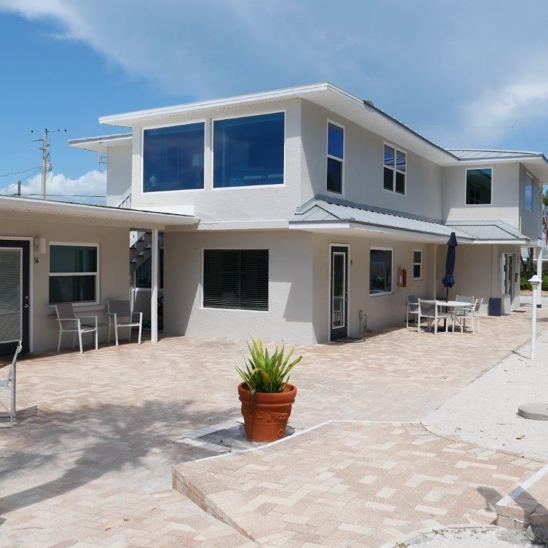 Modern white two-story house with large windows and a paved courtyard under a blue sky