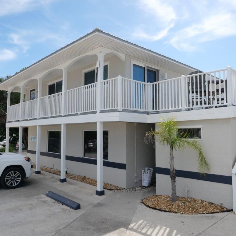 White two-story house with a balcony, carport, and parked car under a blue sky