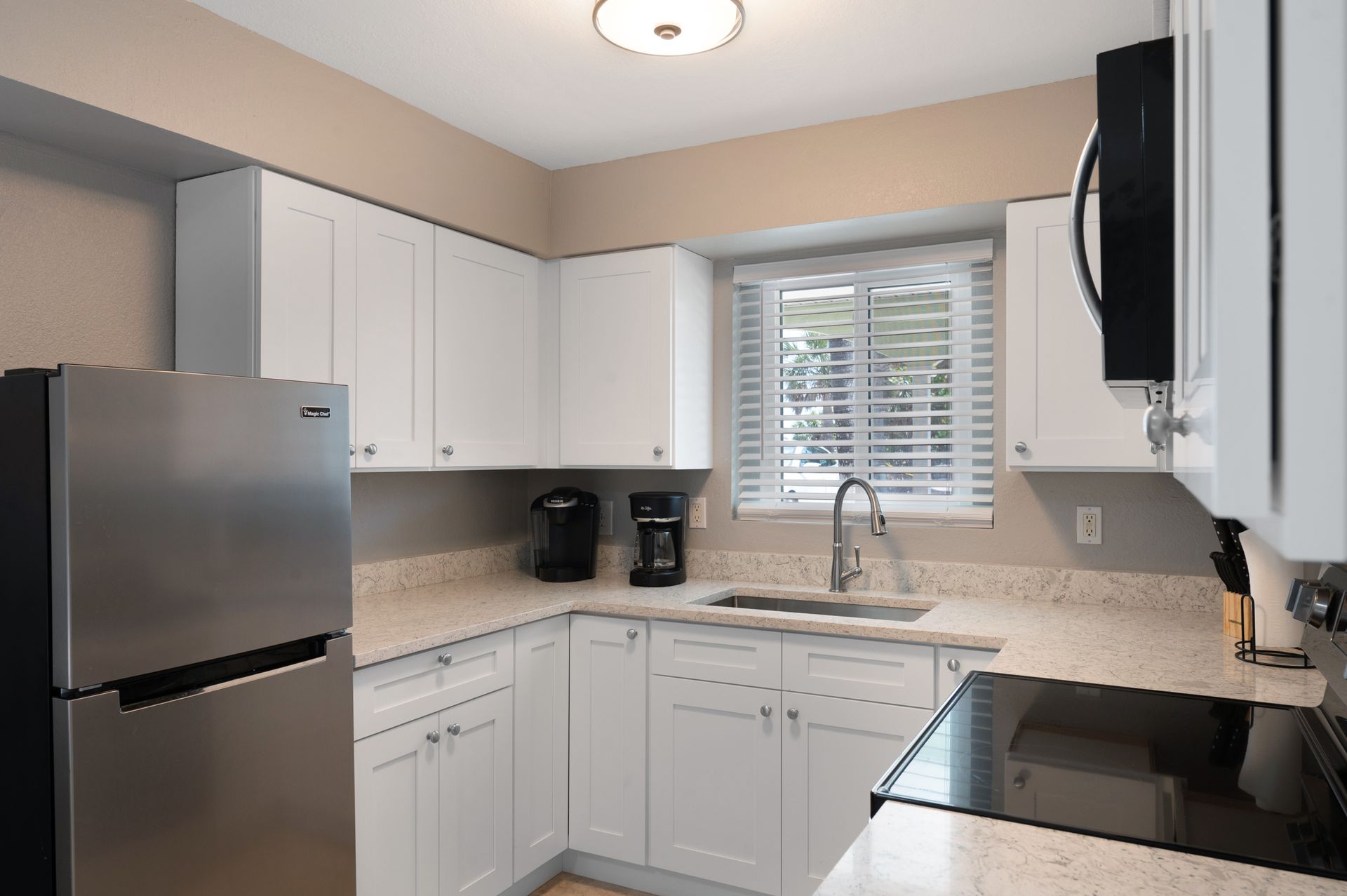 White kitchen with stainless steel refrigerator, white cabinets, countertop, and black appliances.