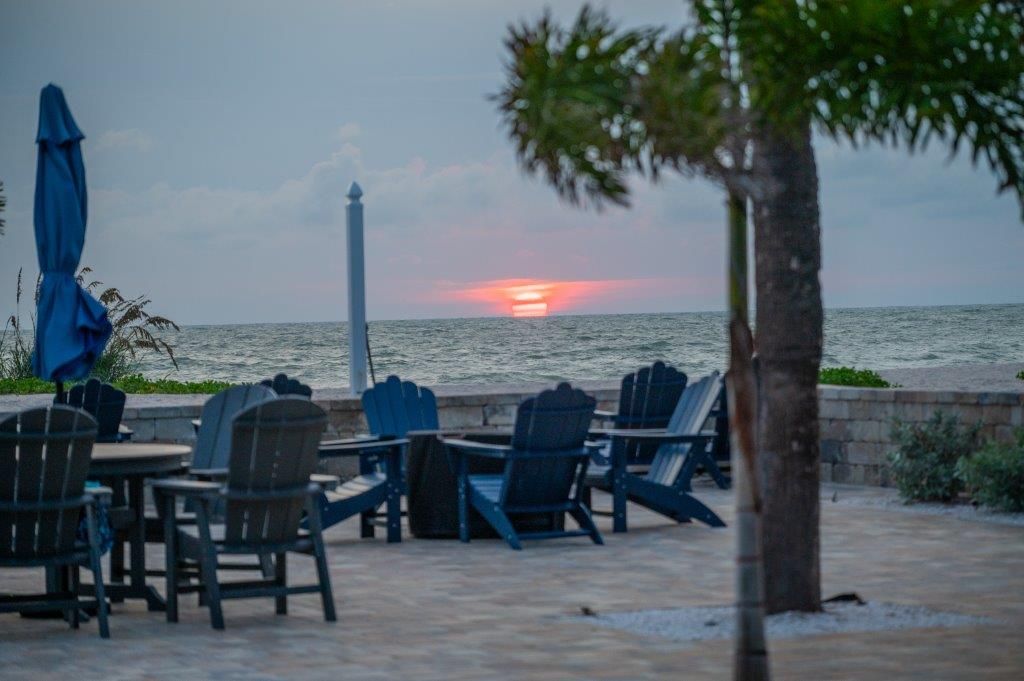 Beachfront patio with empty chairs and closed umbrellas at sunset over the ocean