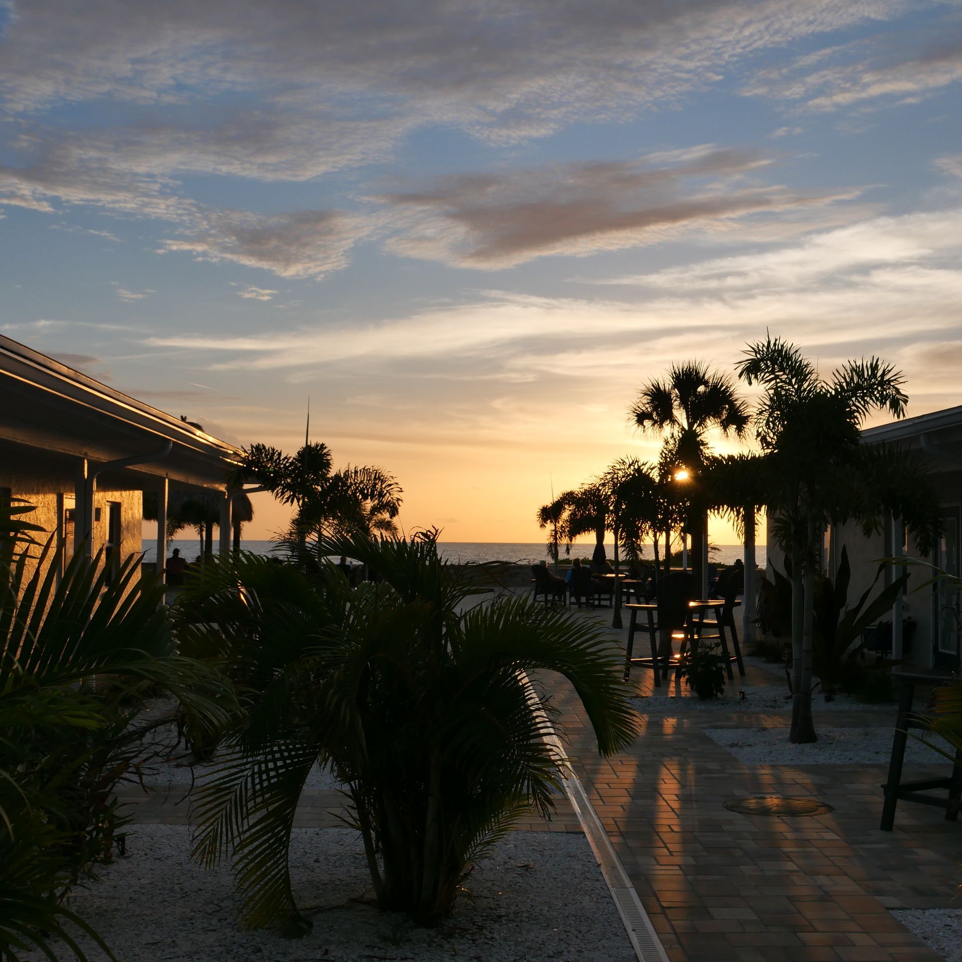 Sunset over a tropical courtyard with palm trees and a wet tiled path between buildings