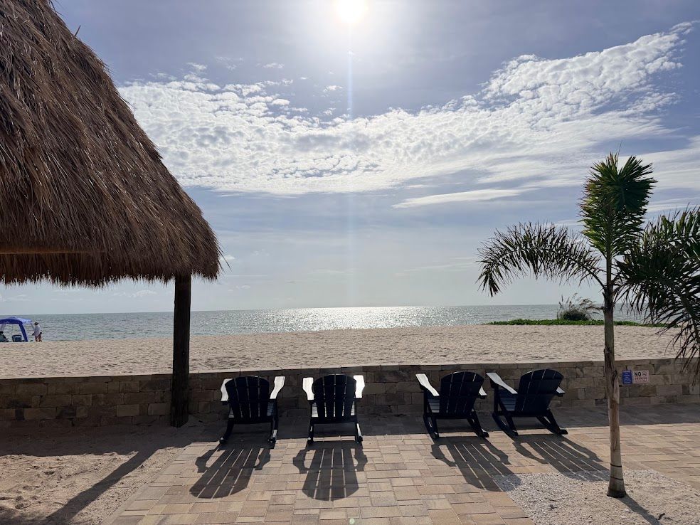 Patio with yellow wall, tables, chairs, teal umbrellas, and ocean view under a cloudy sky
