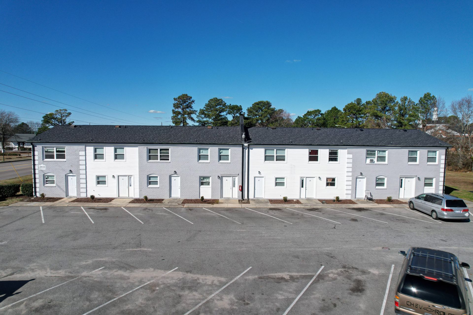 Row of white townhouses with parking lot under a clear blue sky