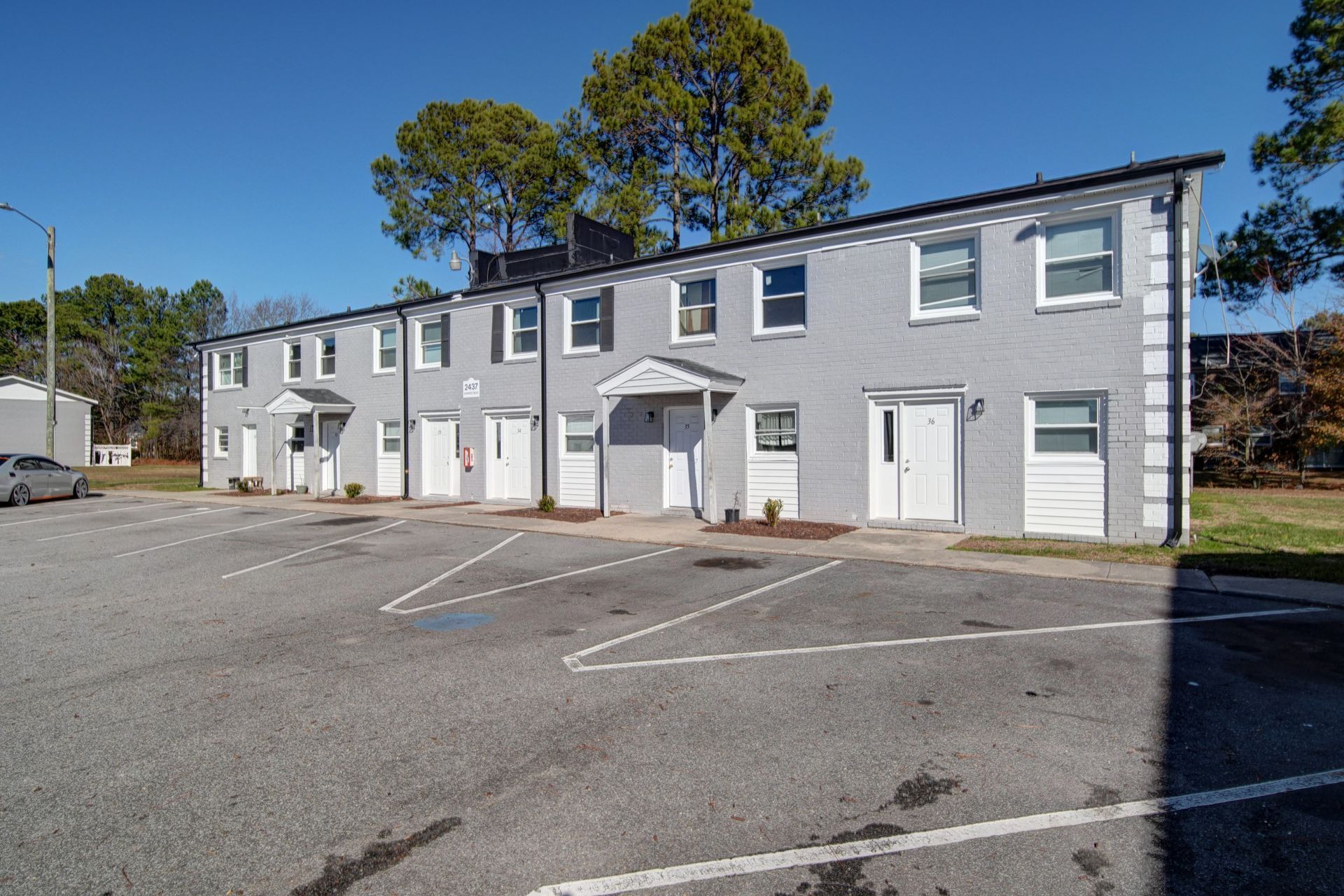 Gray two-story apartment building with white trim and parking lot in front under a blue sky