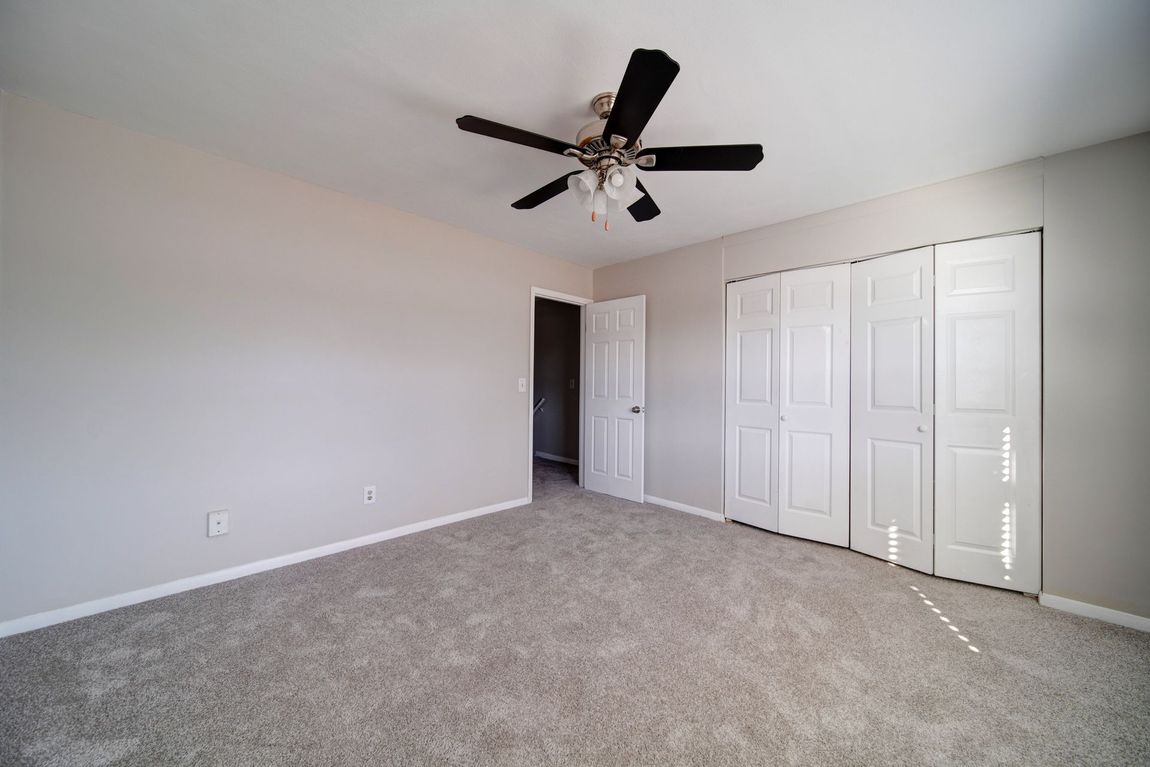 Empty carpeted bedroom with white walls, ceiling fan, and a large closet with sliding doors.