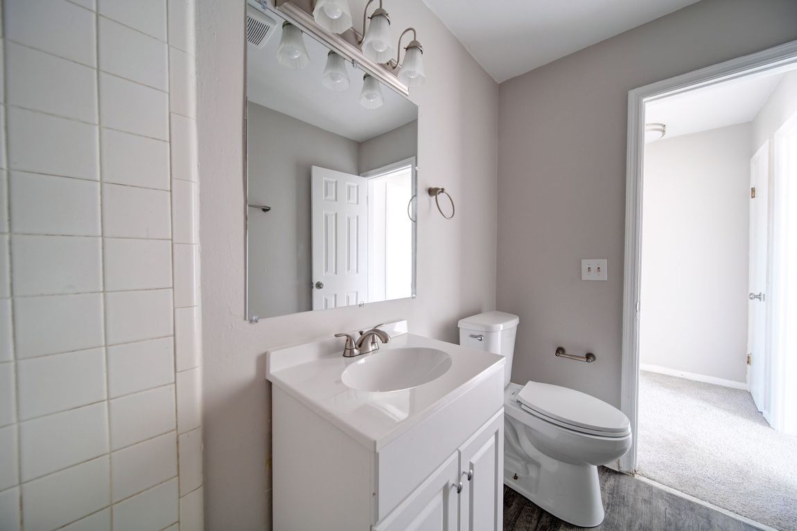Small white bathroom with vanity, mirror, sink, and toilet beside a tiled shower or tub area.