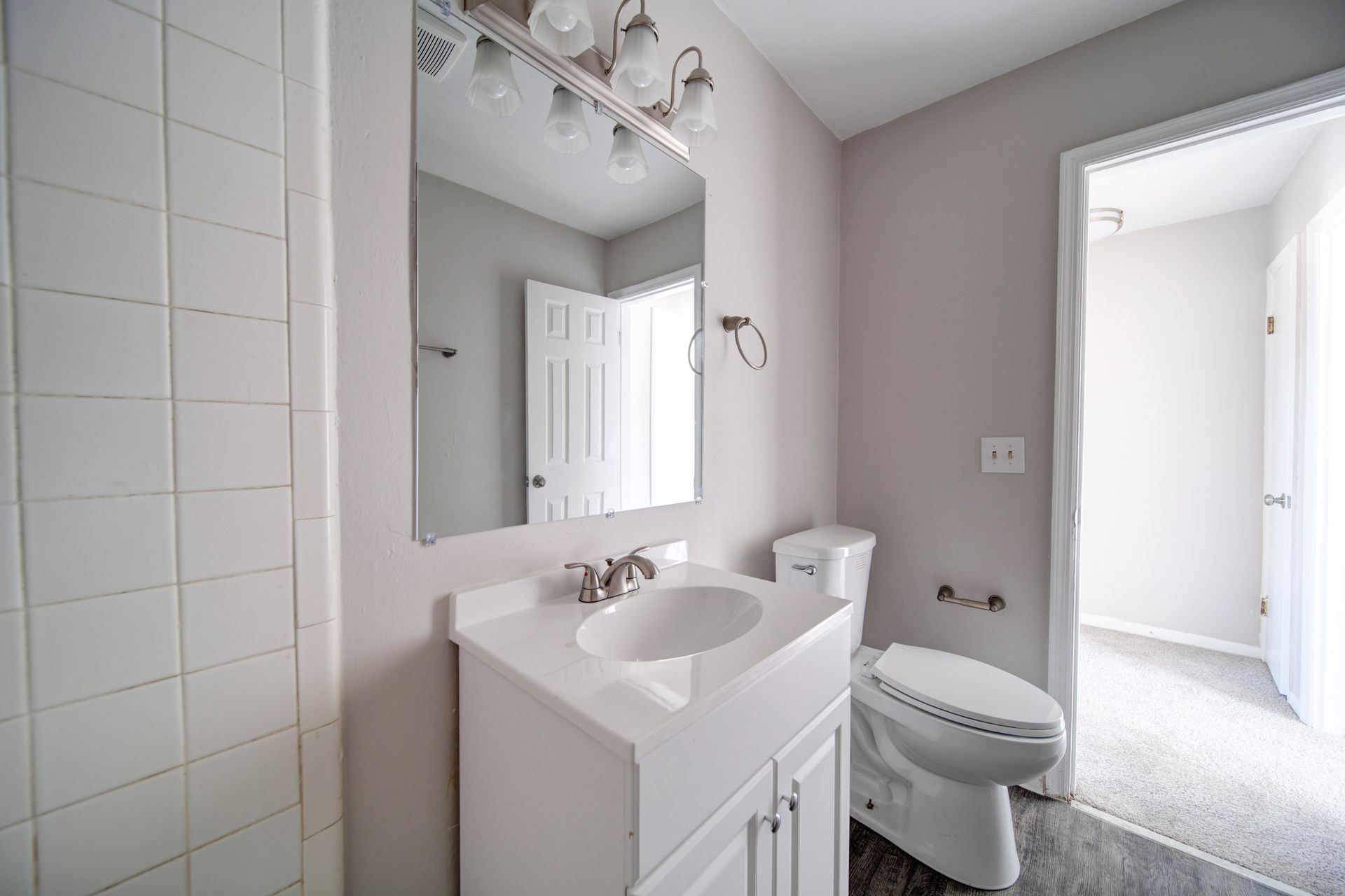 Small white bathroom with vanity, mirror, sink, and toilet beside a tiled shower or tub area.
