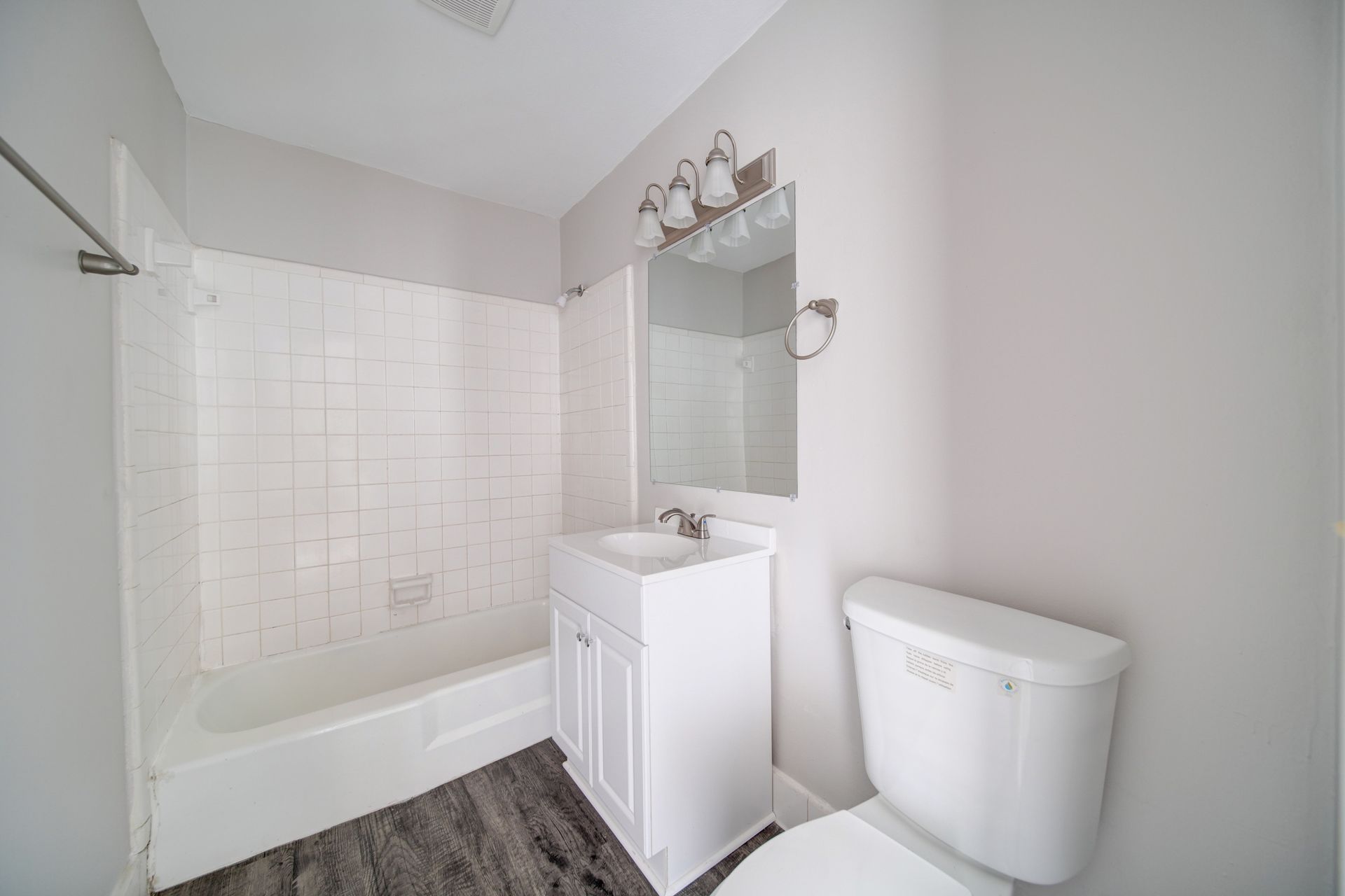 Bright white bathroom with tub-shower, vanity sink, mirror, and toilet on a gray floor.