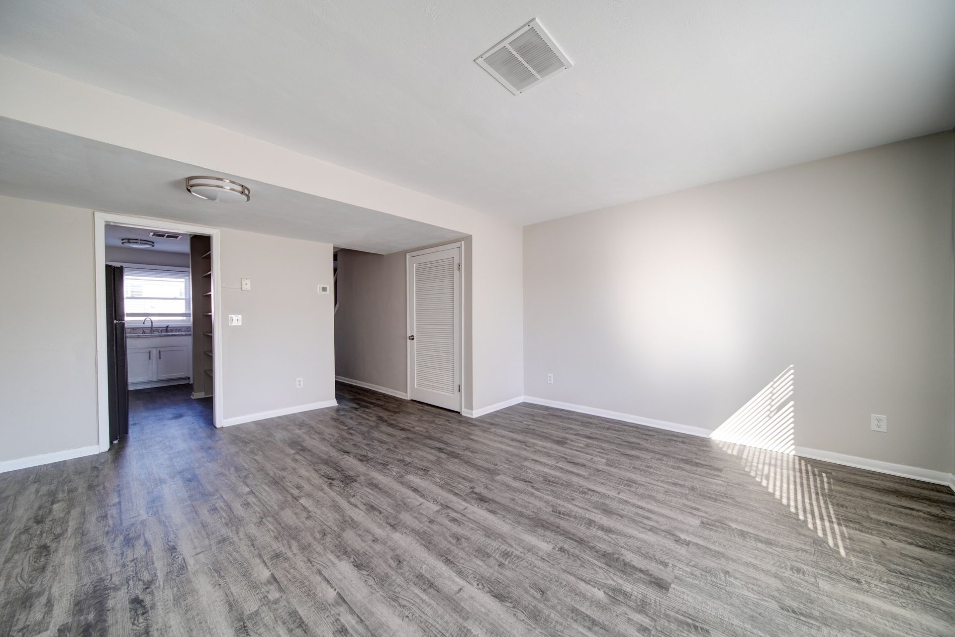 Empty gray room with wood-look flooring, white walls, and bright sunlight from the right window.