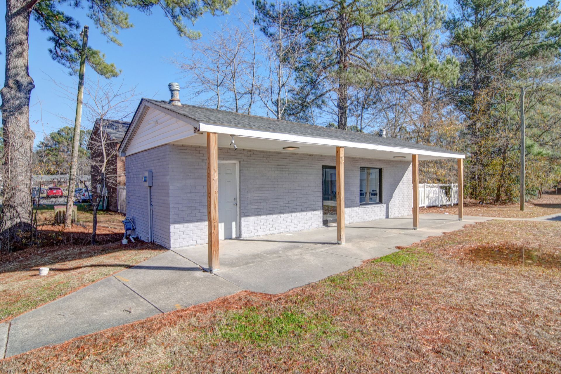 Small white house with a covered front porch and concrete driveway in a wooded yard