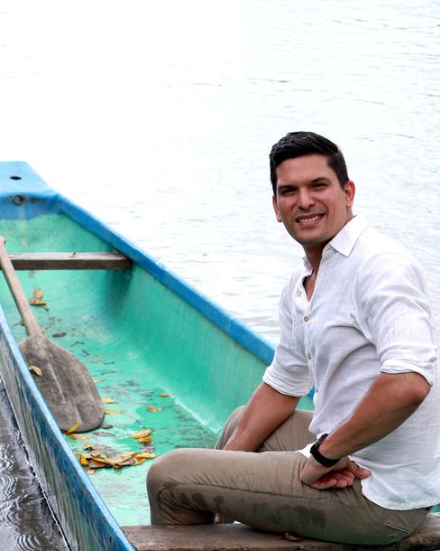 Un hombre sentado en una barca de color turquesa sobre el agua, sonriendo a la cámara