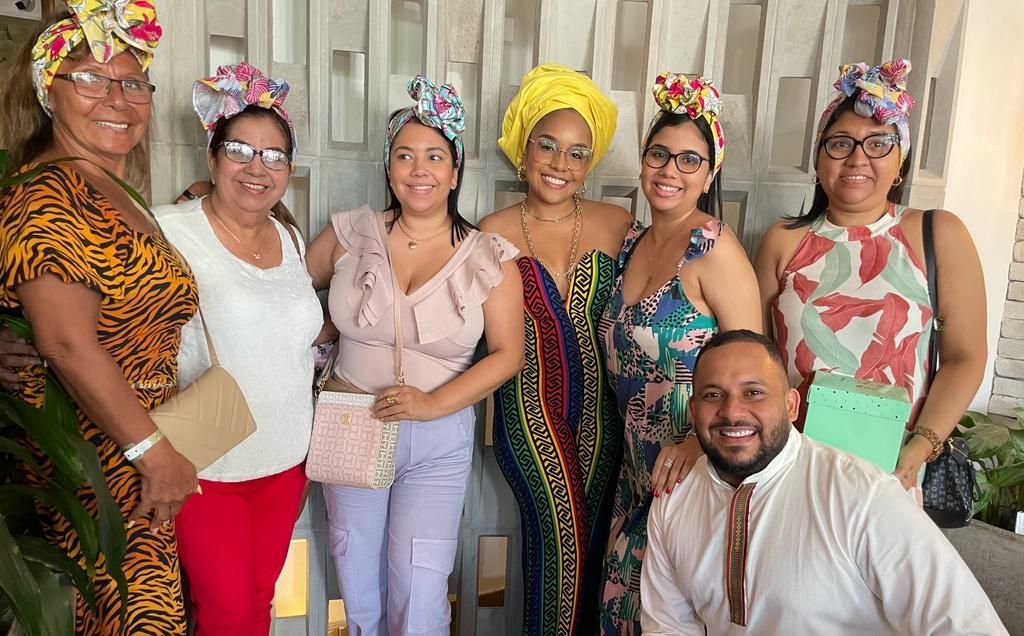 Un grupo de personas sonríen en el interior de un edificio, luciendo coloridos tocados florales