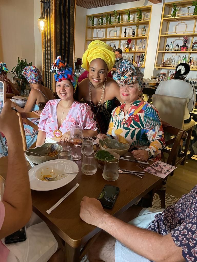 Cuatro personas con coloridos pañuelos en la cabeza están sentadas a la mesa de un restaurante con platos
