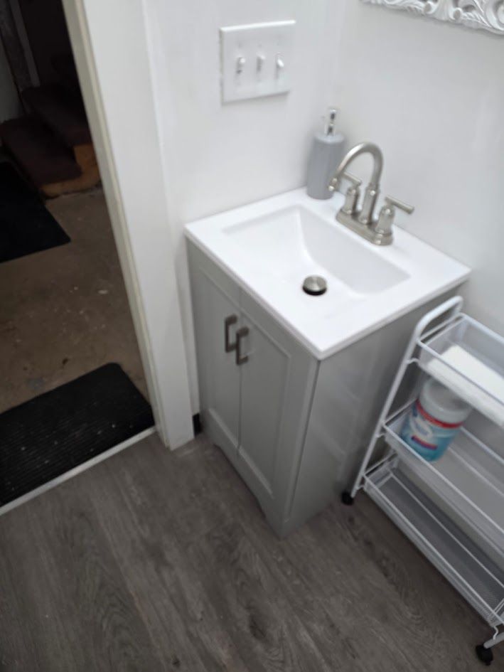 Small white bathroom sink cabinet beside a hallway, with a chrome faucet and a metal shelf cart nearby
