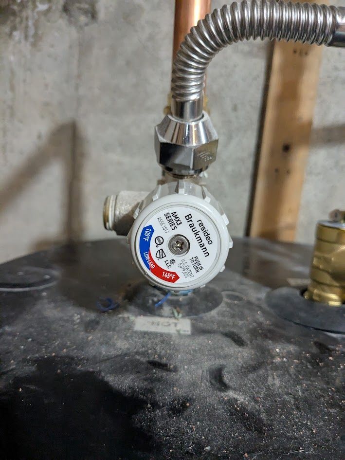Gas meter with a flexible metal hose mounted on a dusty black tank in a utility area.