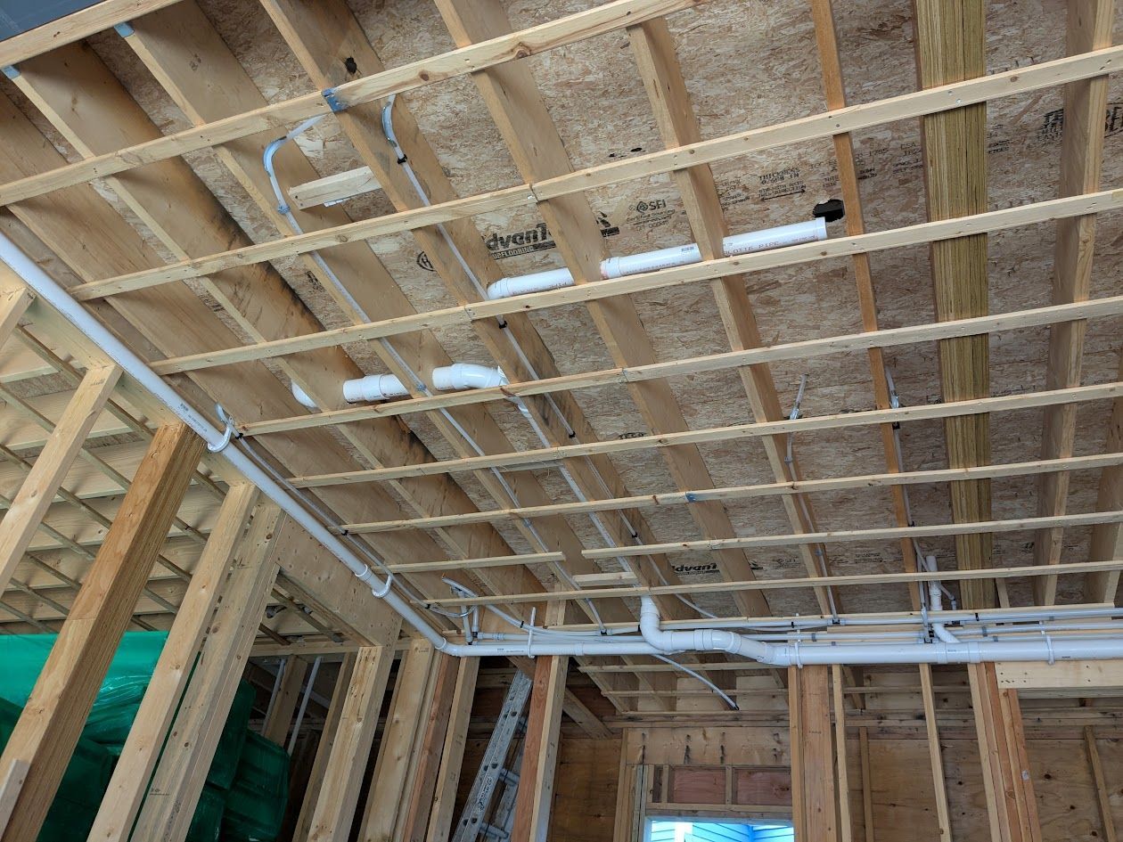 Interior of a wooden-framed house under construction, showing roof trusses and wall studs.