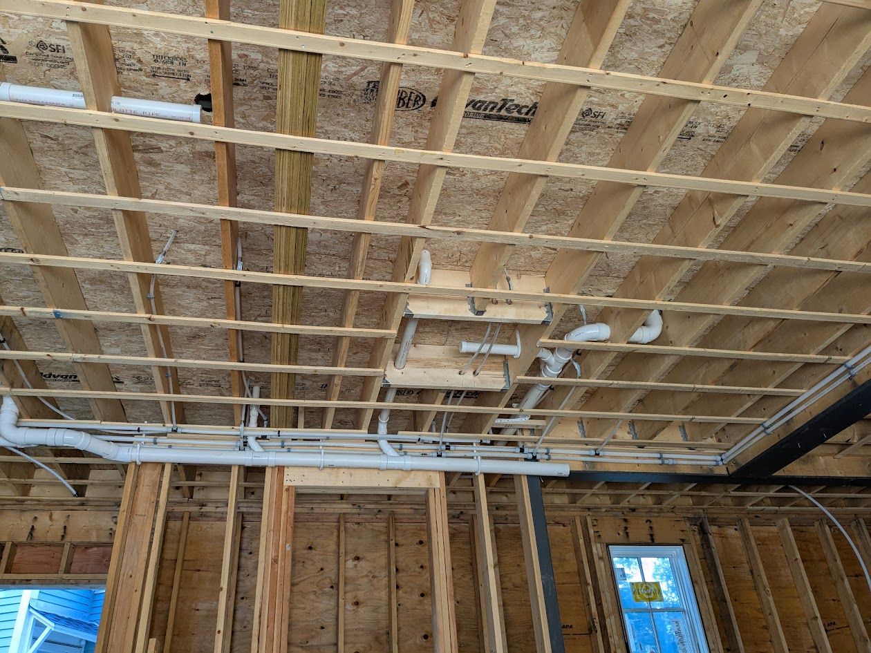 Exposed ceiling framing in an unfinished room with insulation and a window in the background