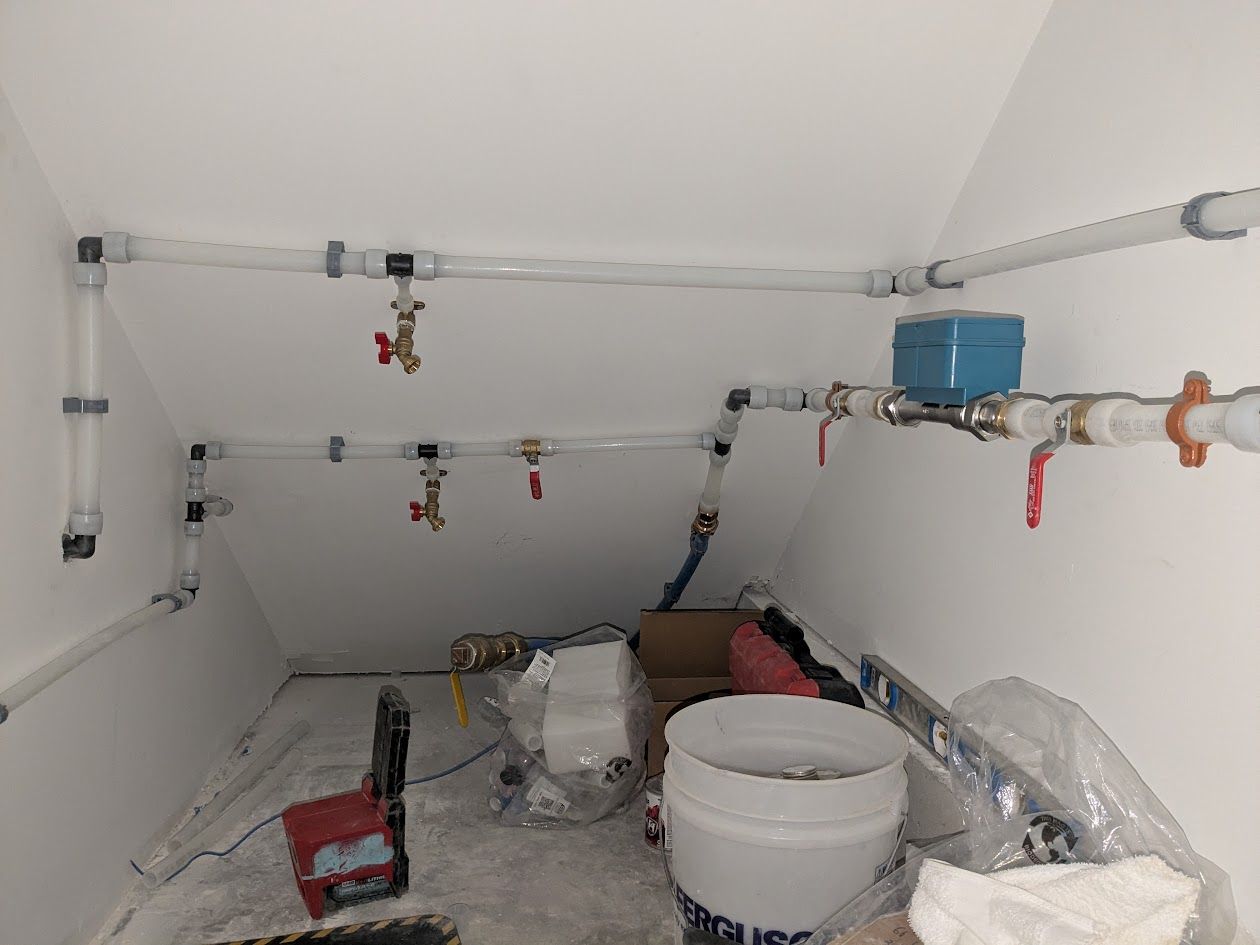 Small utility room with white pipes, valves, and buckets on the floor, likely a plumbing area.
