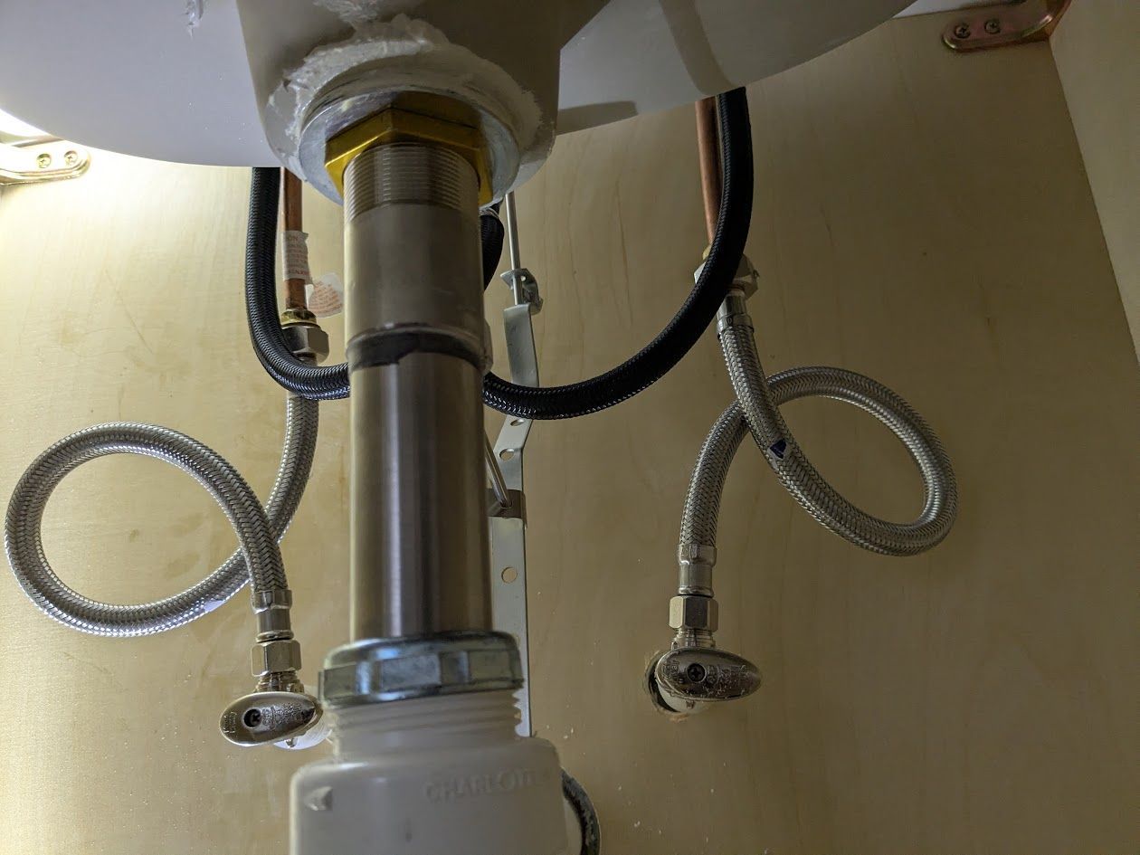 Chrome sink drain pipe with two flexible braided water lines under a sink