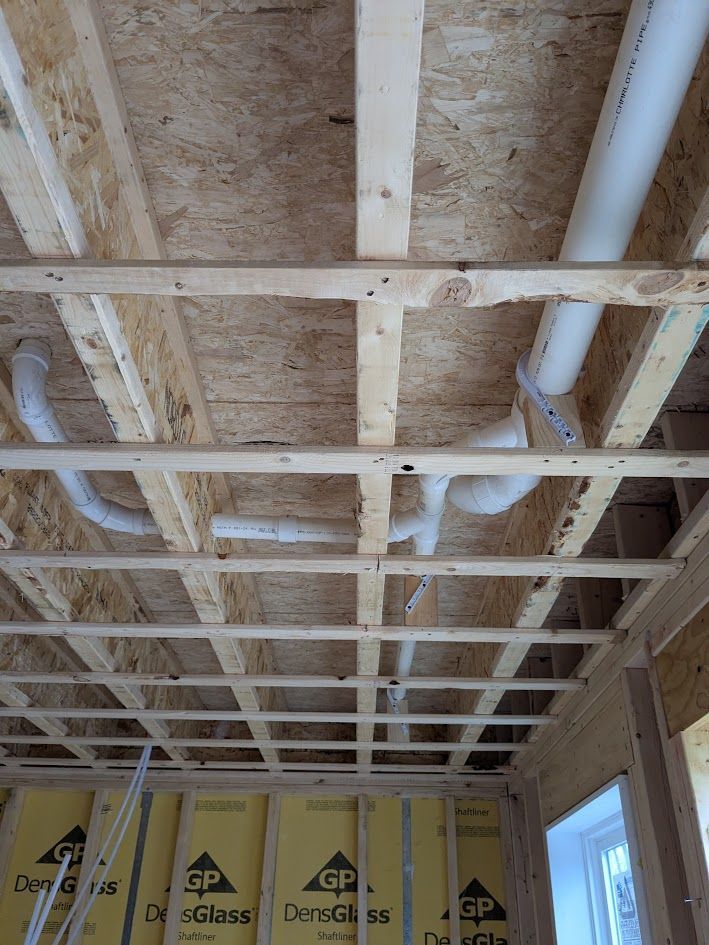 Exposed wood ceiling framing with white pipes and insulation above unfinished interior walls