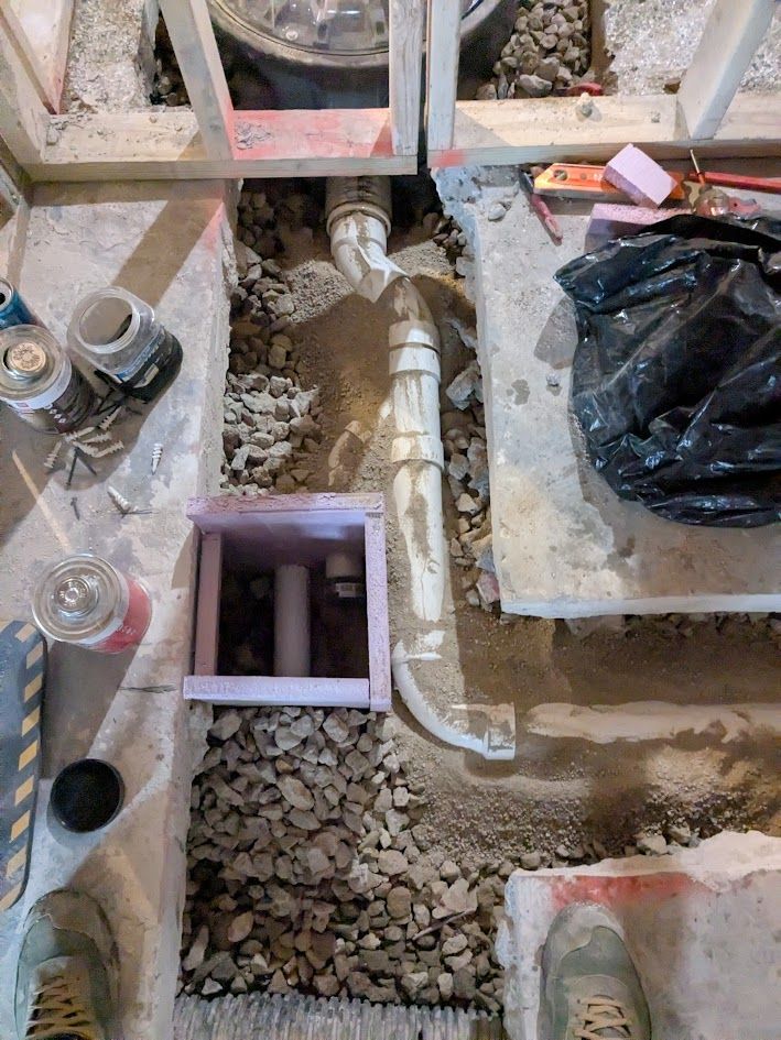 Construction site with exposed plumbing pipes and gravel around a floor opening