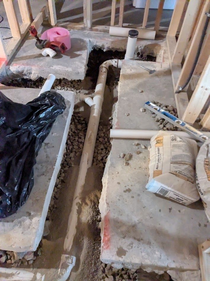 Construction site floor with exposed plumbing pipes and concrete slabs in a framed room