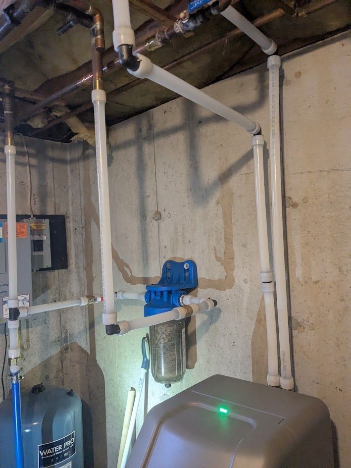 Basement utility area with white pipes, a blue valve, and a water filter tank against a concrete wall