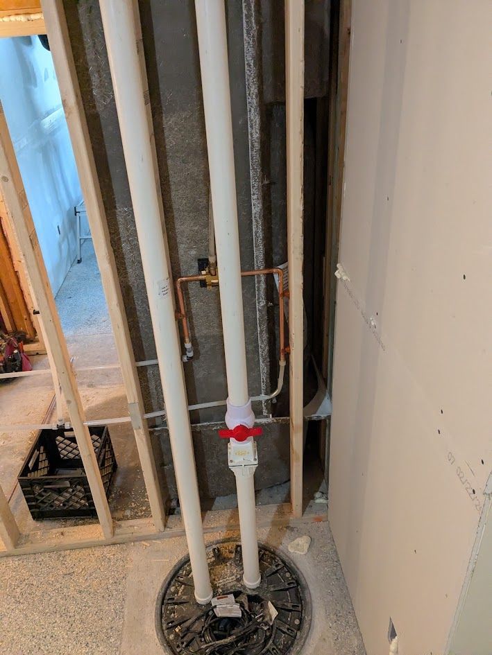 Exposed plumbing pipes in an unfinished interior wall with a red valve and open studs.