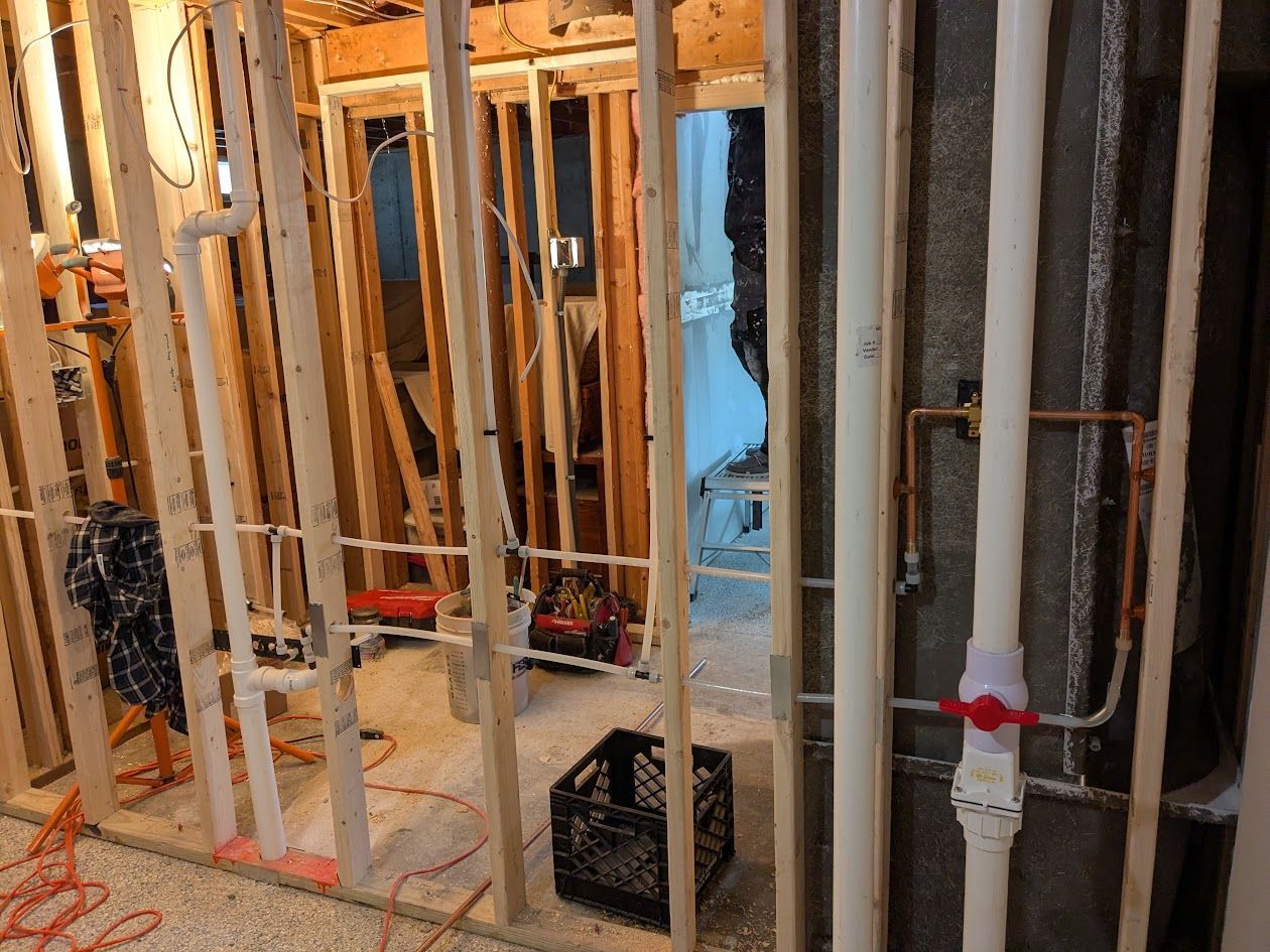 Framed interior under construction with exposed studs, plumbing pipes, and unfinished walls.