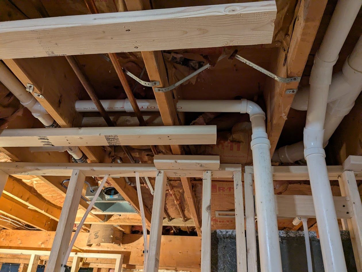 Exposed ceiling framing and white plumbing pipes in an unfinished interior construction area