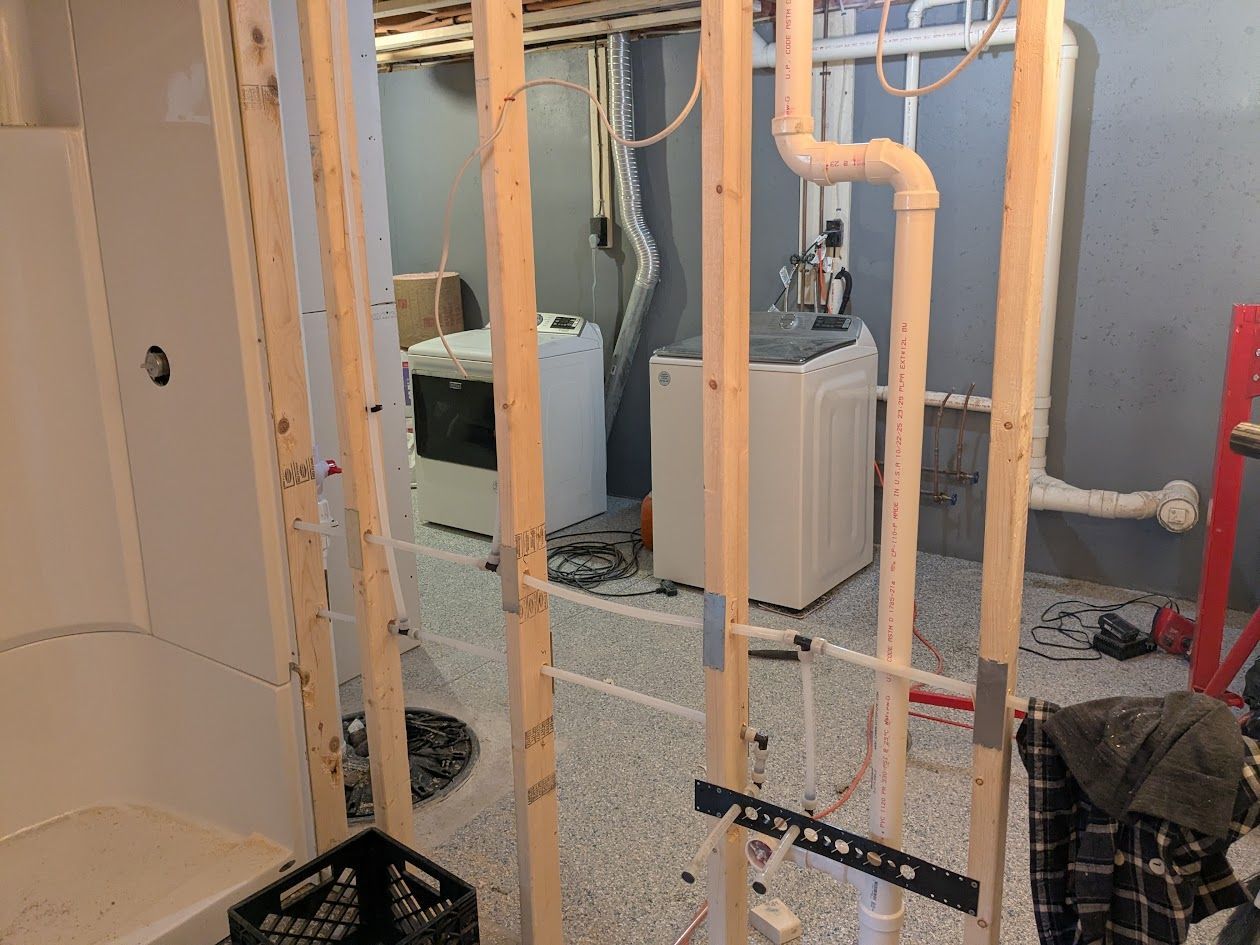 Unfinished basement framing with exposed plumbing, HVAC units, and a shower/tub alcove under construction