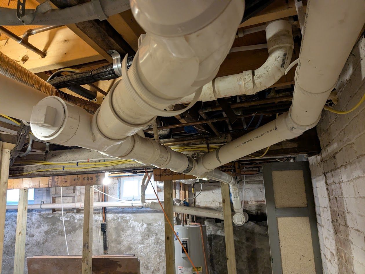 Basement ceiling with exposed white pipes, ductwork, and wiring above concrete walls