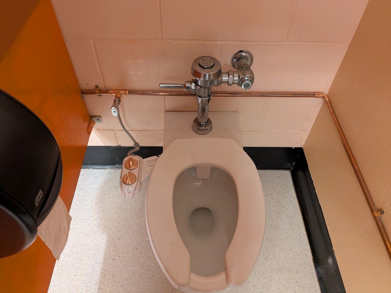 Public restroom toilet with open seat and metal flush valve, viewed from above.