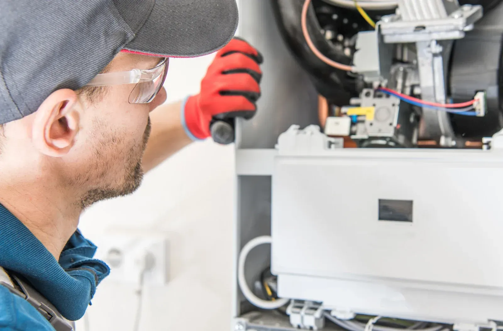 Technician inspecting open electrical equipment with tools and red gloves