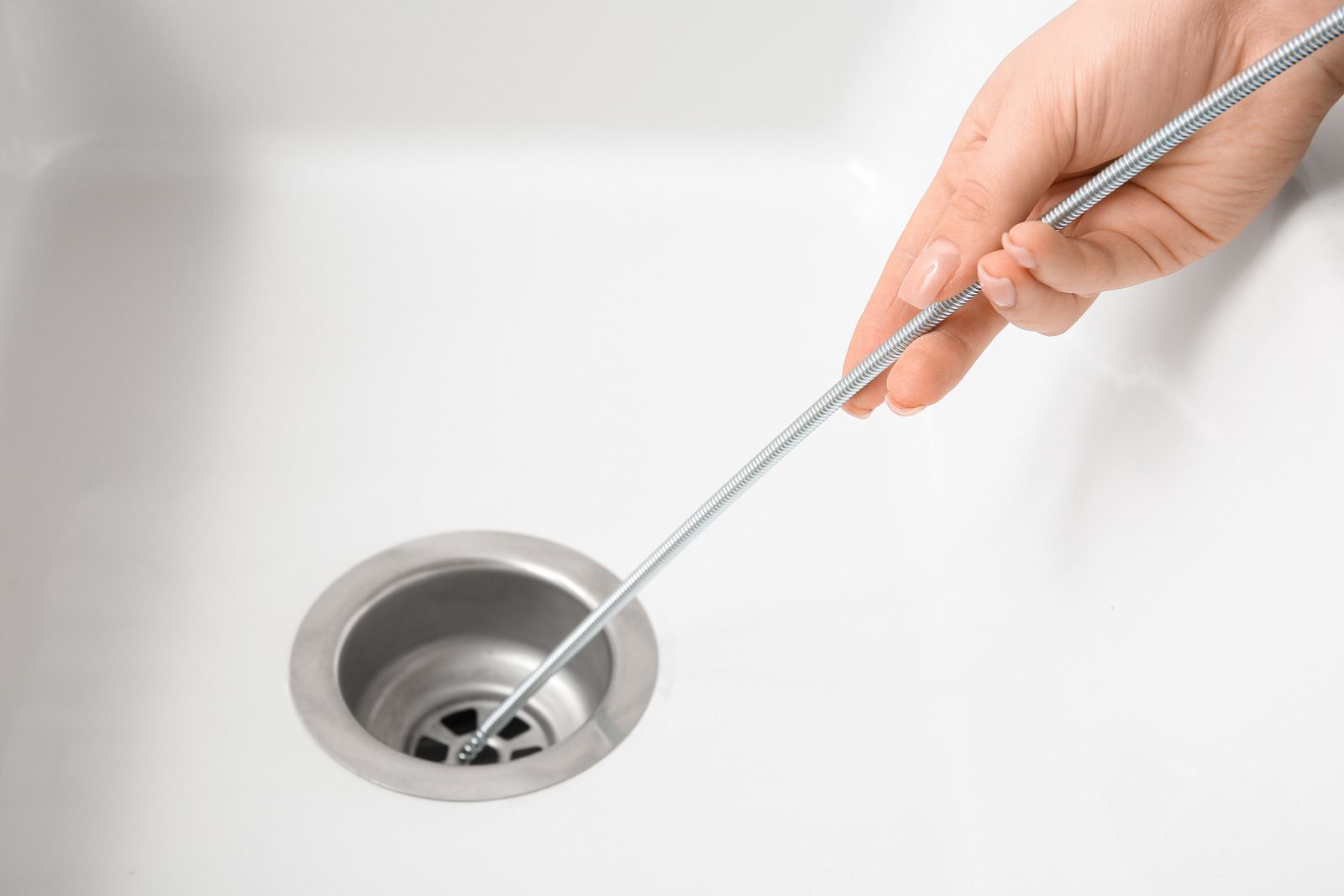 Hand using a drain cleaning tool in a bathroom sink drain
