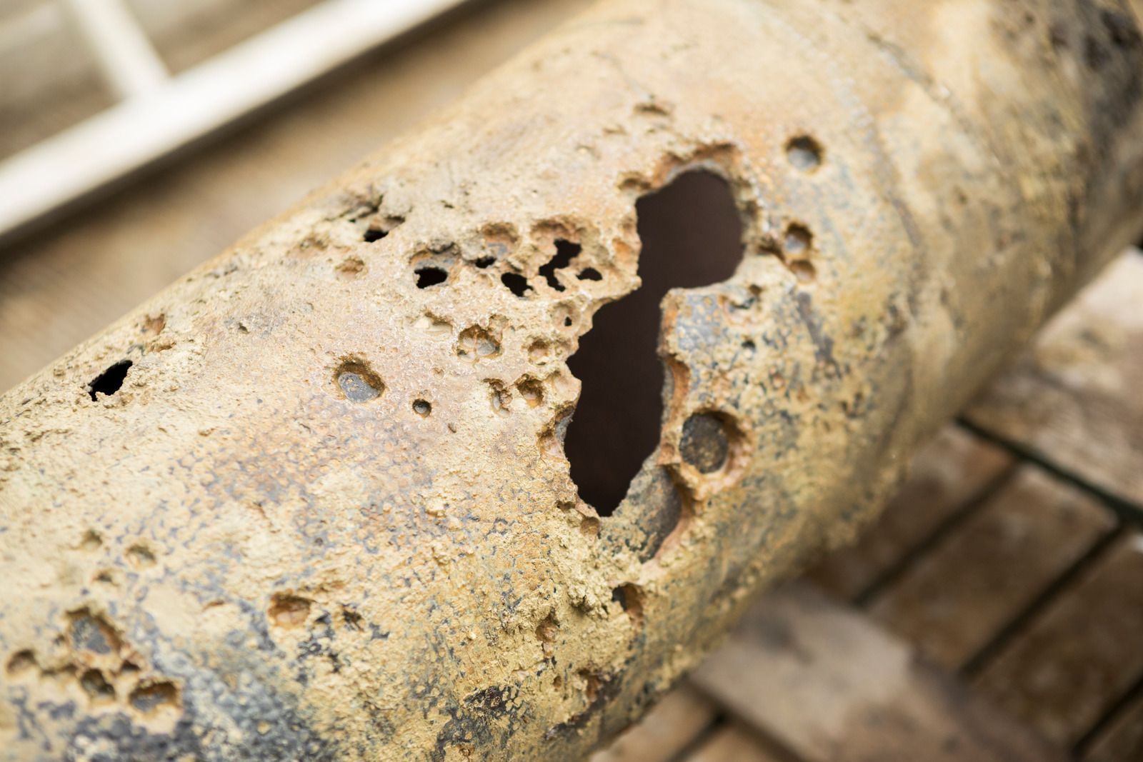 Rusty metal pipe with a large hole and pitted corrosion close-up
