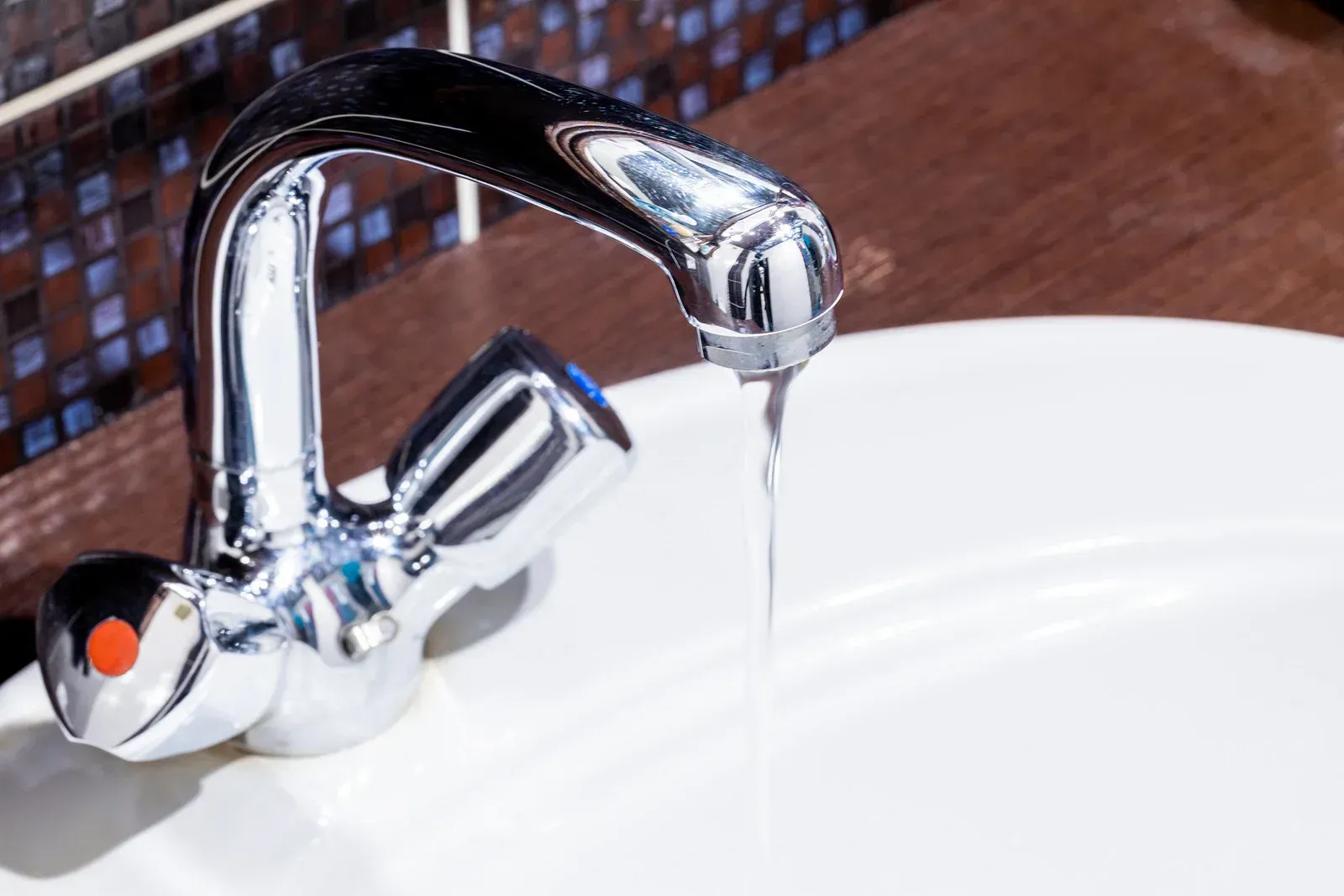 Chrome faucet running water over a white sink