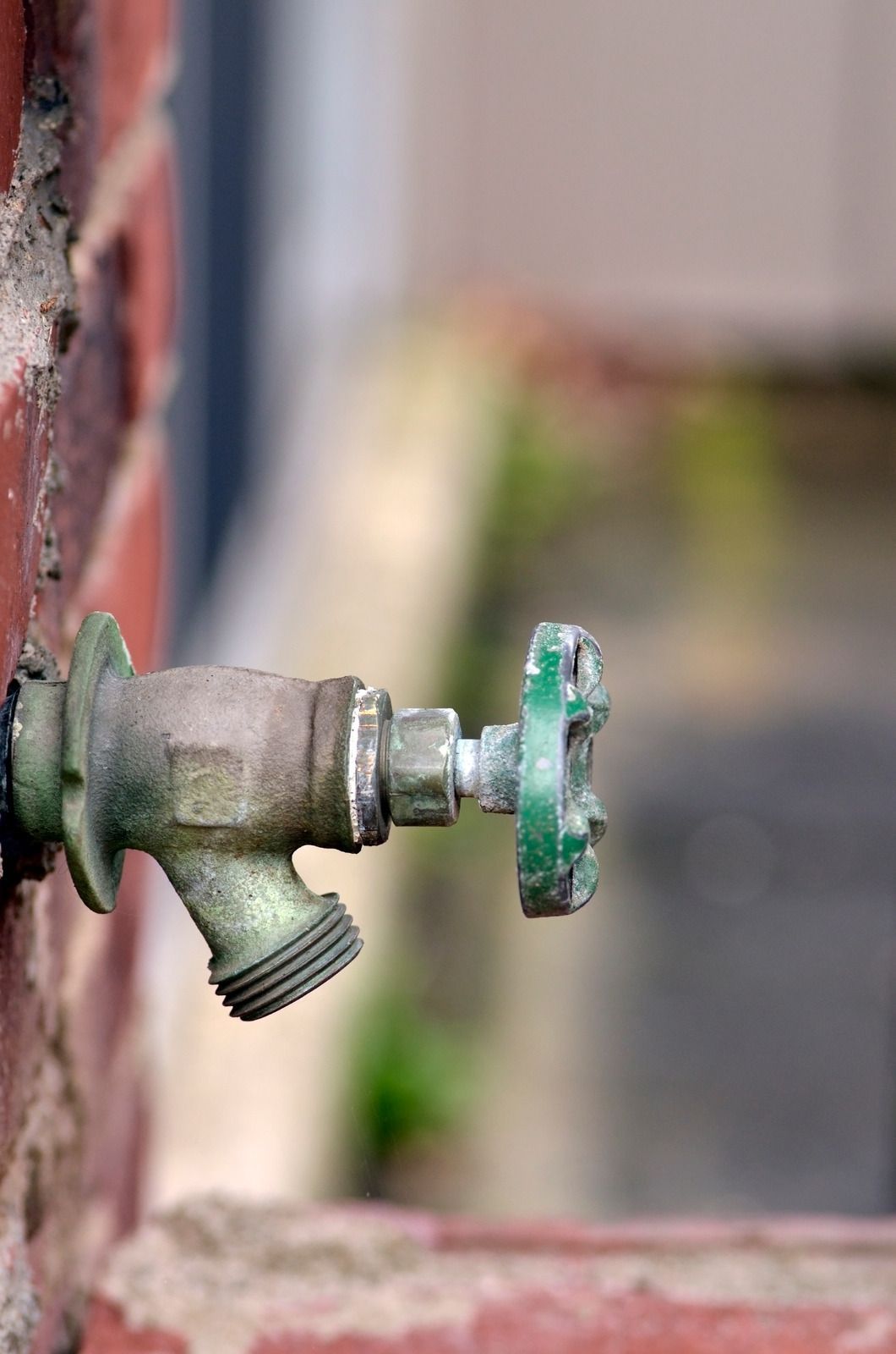 Outdoor metal faucet protruding from a wall, with a green valve handle and threaded spout.