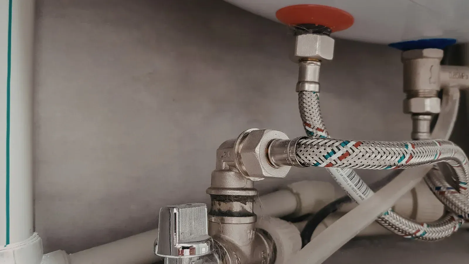 Under-sink plumbing with braided hoses and shutoff valves against a gray cabinet wall