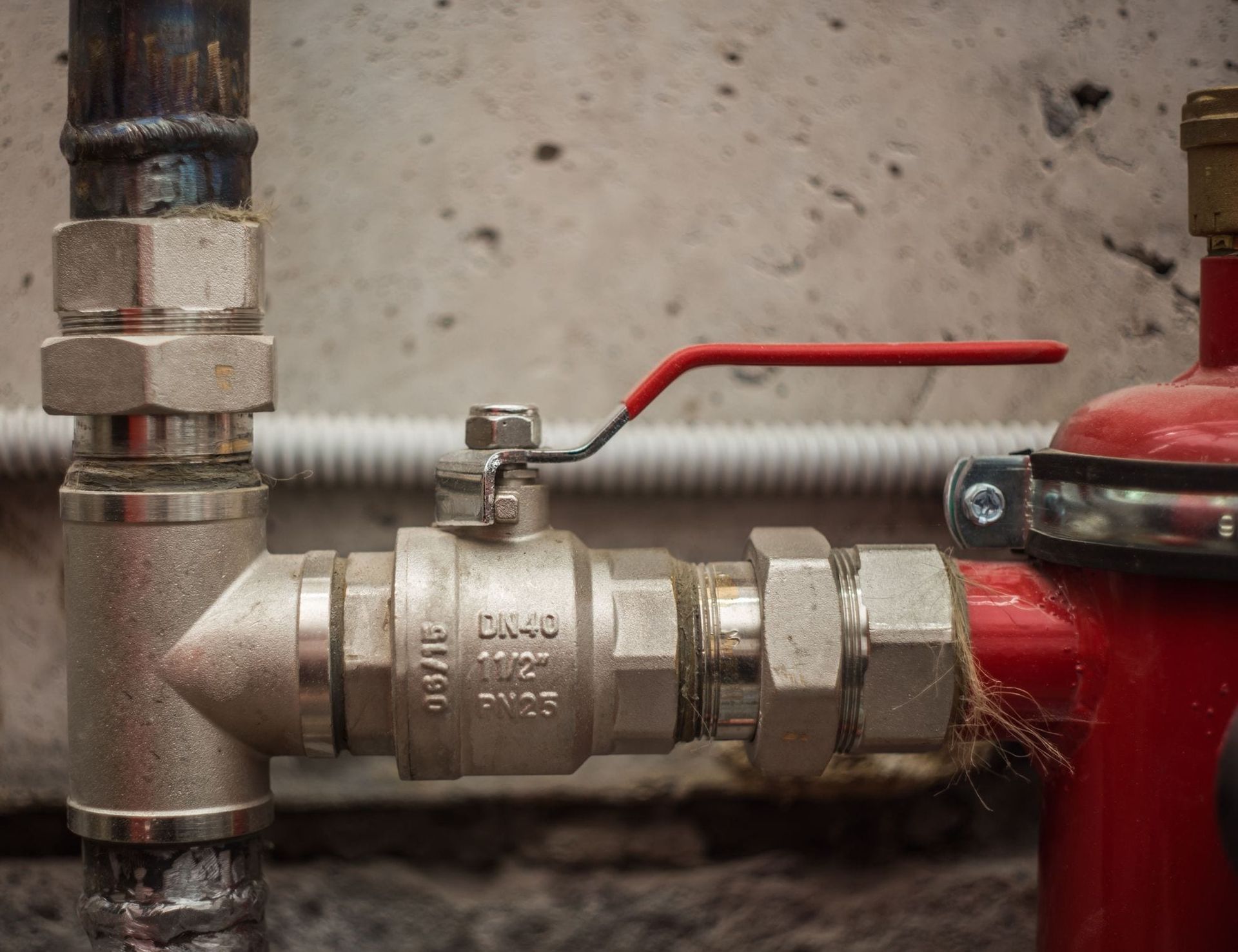 A close up of a valve on a pipe with a red handle.