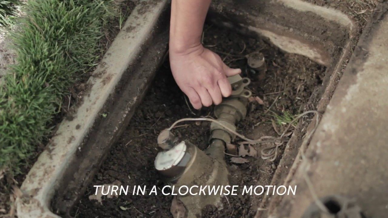 A person is reaching for a water meter in the dirt.